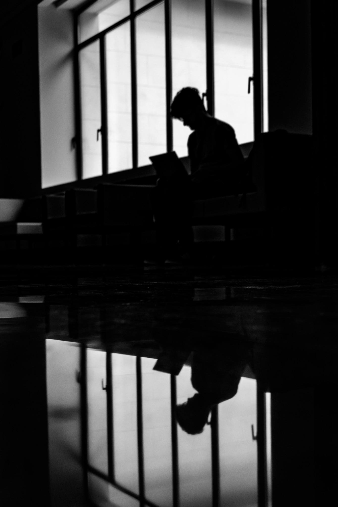 Una persona sentada junto a los ventanales y su reflejo